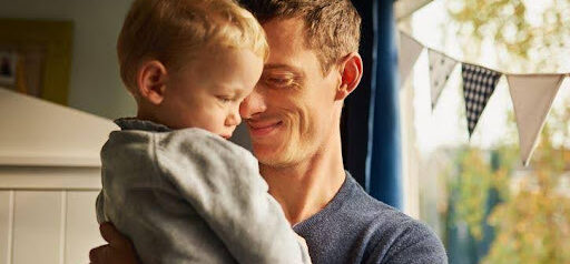 father smiles as he holds son in his arms while standing in backyard KHM Attorneys at Law Colorado Springs, Castle Rock