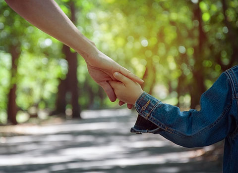 child holds parent's hand while walking down path with trees KHM Attorneys at Law Colorado Springs, Castle Rock